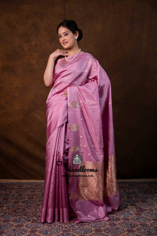 Woman wearing a purple saree with gold patterns against a brown background